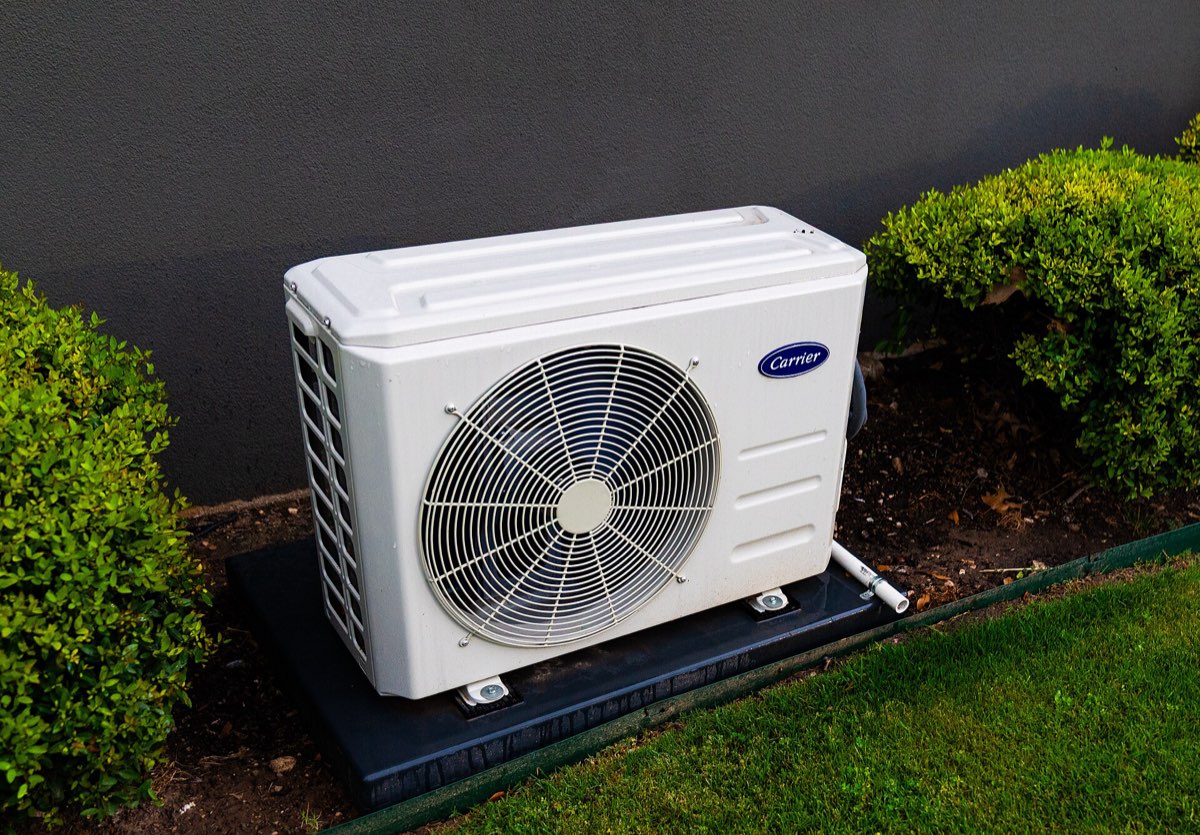 Outdoor heat pump unit on a pad between garden hedges
